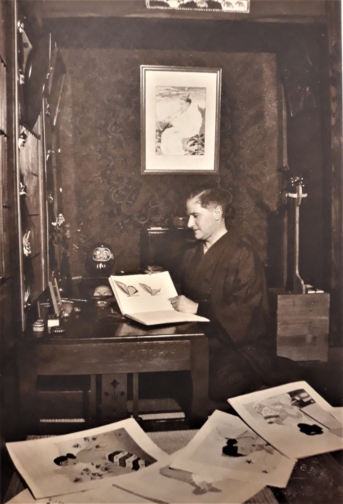 Paul Jacoulet at home in March 1938 looking at a book on butterflies, his Shamisen behind him. We recognize several prints : hung on the wall the Hokkan Zan of 1937 and scattered Le rocher de Jokadj of 1936, Le Marchand de sel of 1936, Une belle de Palaos from 1935 and Le miroir de laque rouge from February 1938, just recently completed.